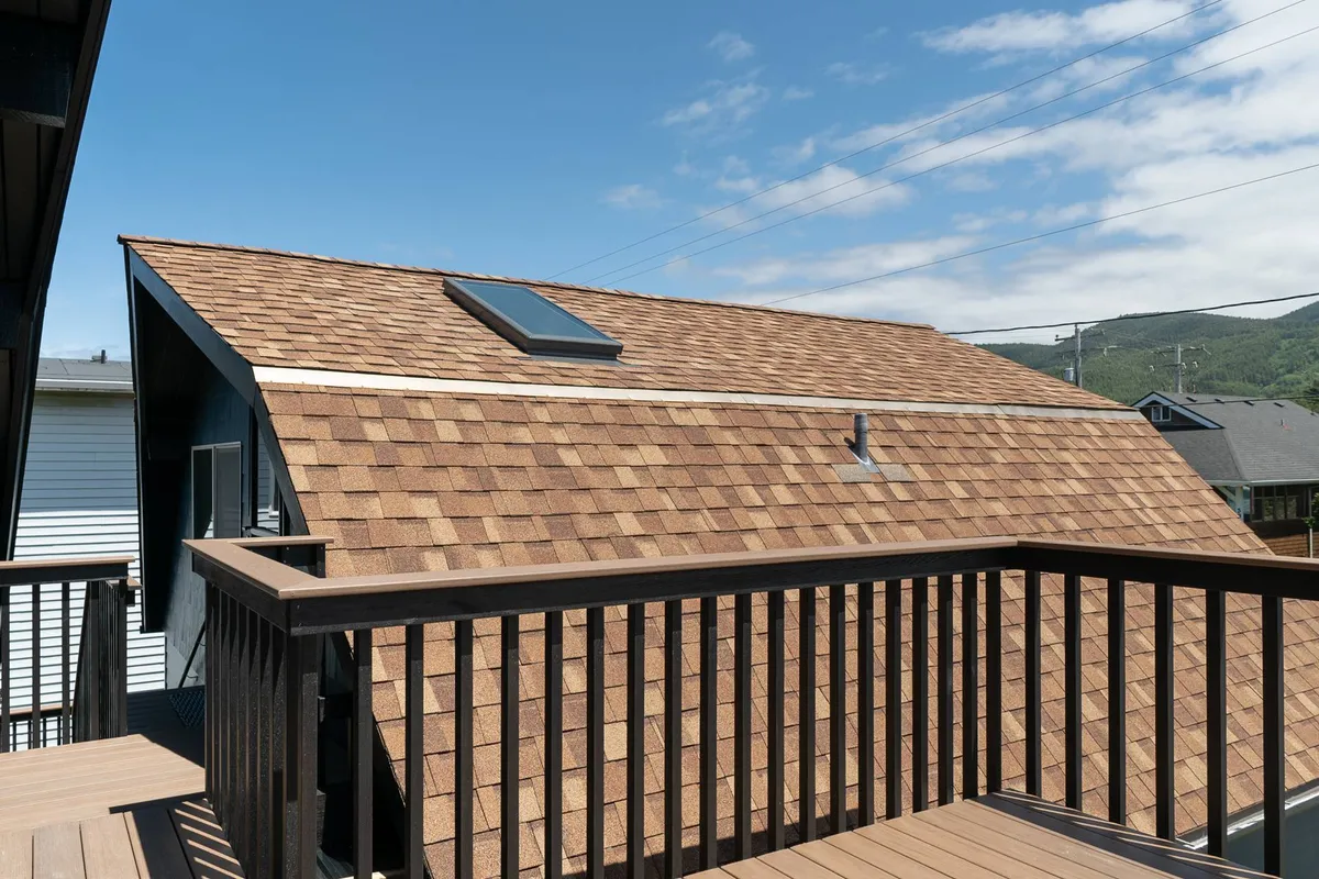 This exterior shot focuses on a peaceful deck with shingled roofing and railings that overlook serene skies. The space is designed for relaxation or social gatherings, with ample room to enjoy fresh ocean air.