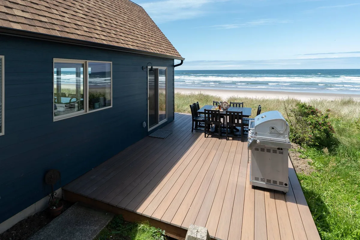 A welcoming deck features a dining table and grill, set against a panoramic backdrop of the Pacific Ocean. The tranquil ambiance is perfect for morning coffee or sharing a sunset dinner with friends, echoing the retreat’s social and relaxing vibe.