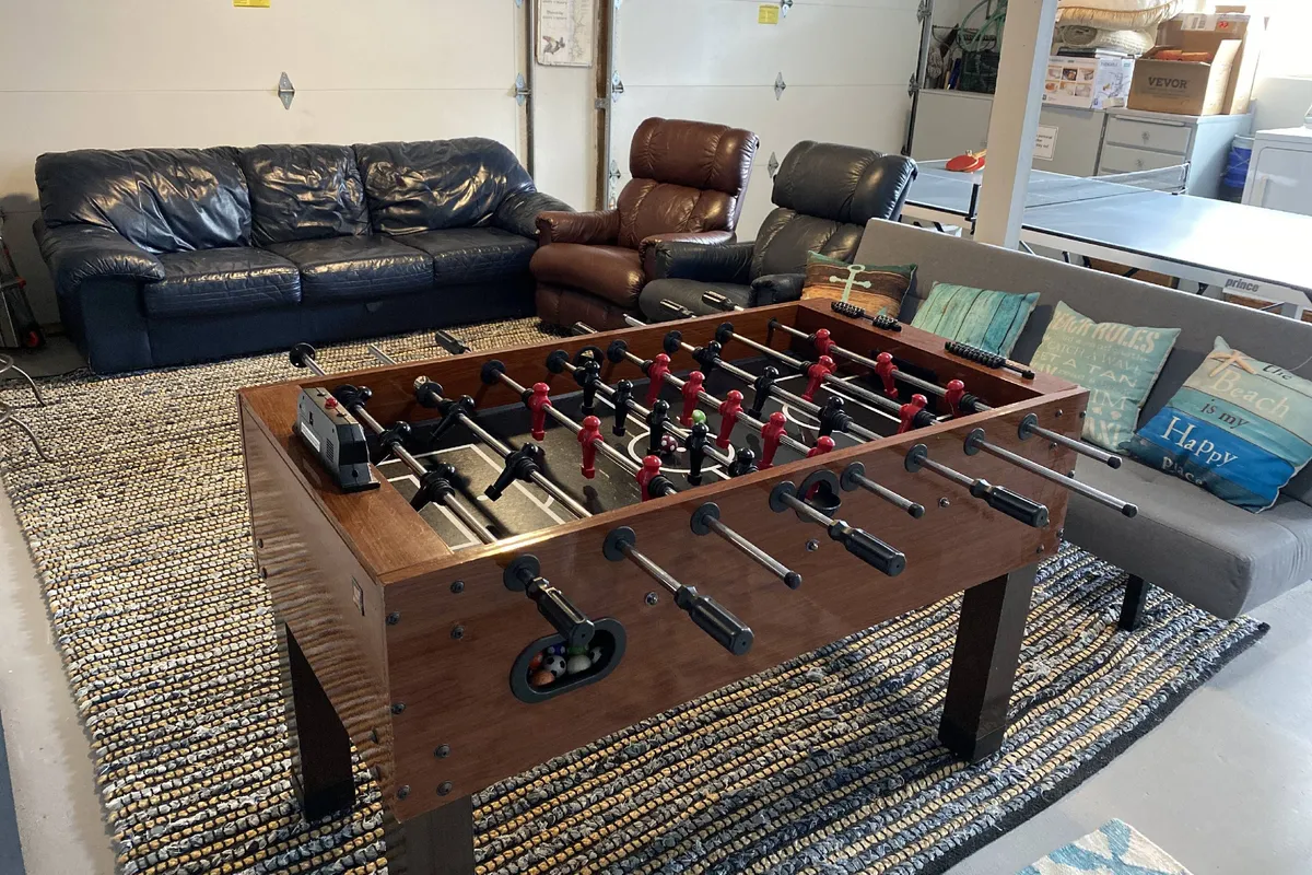 The interior garage game room is shown, featuring a foosball table, comfortable sofas, and a rug. The space is set up for both playful competitions and cozy movie nights, capturing the social and inviting mood.