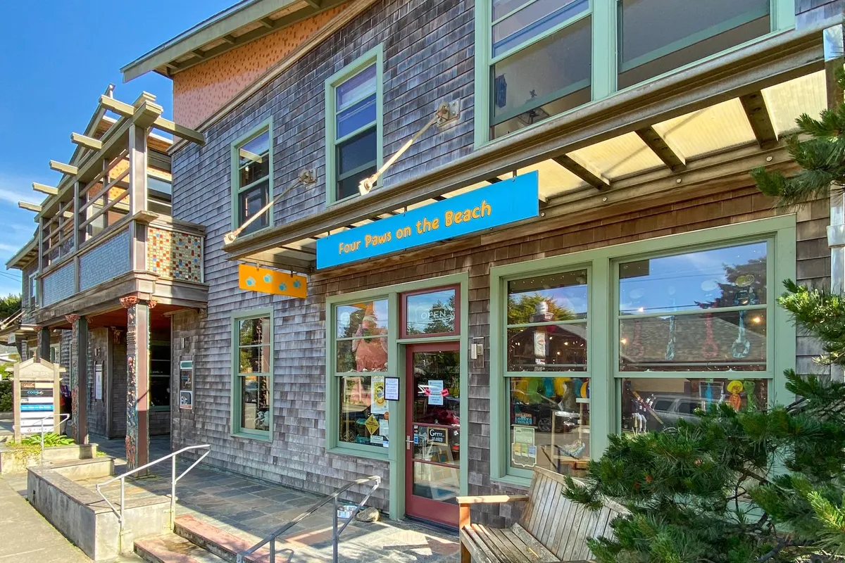 The storefront 'Four Paws on the Beach' featuring a shingled exterior with large windows, inviting pet owners to shop for supplies. The scene is friendly and welcoming, capturing a vibrant pet-friendly atmosphere near the beach.