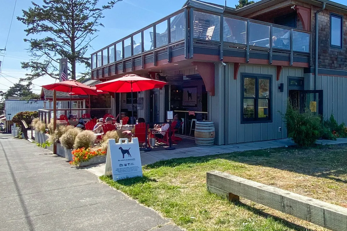 The image features outdoor seating shaded by red umbrellas, with signage reflecting a casual, pet-friendly café atmosphere. The inviting setup suggests a place for socializing and enjoying meals in the open air.