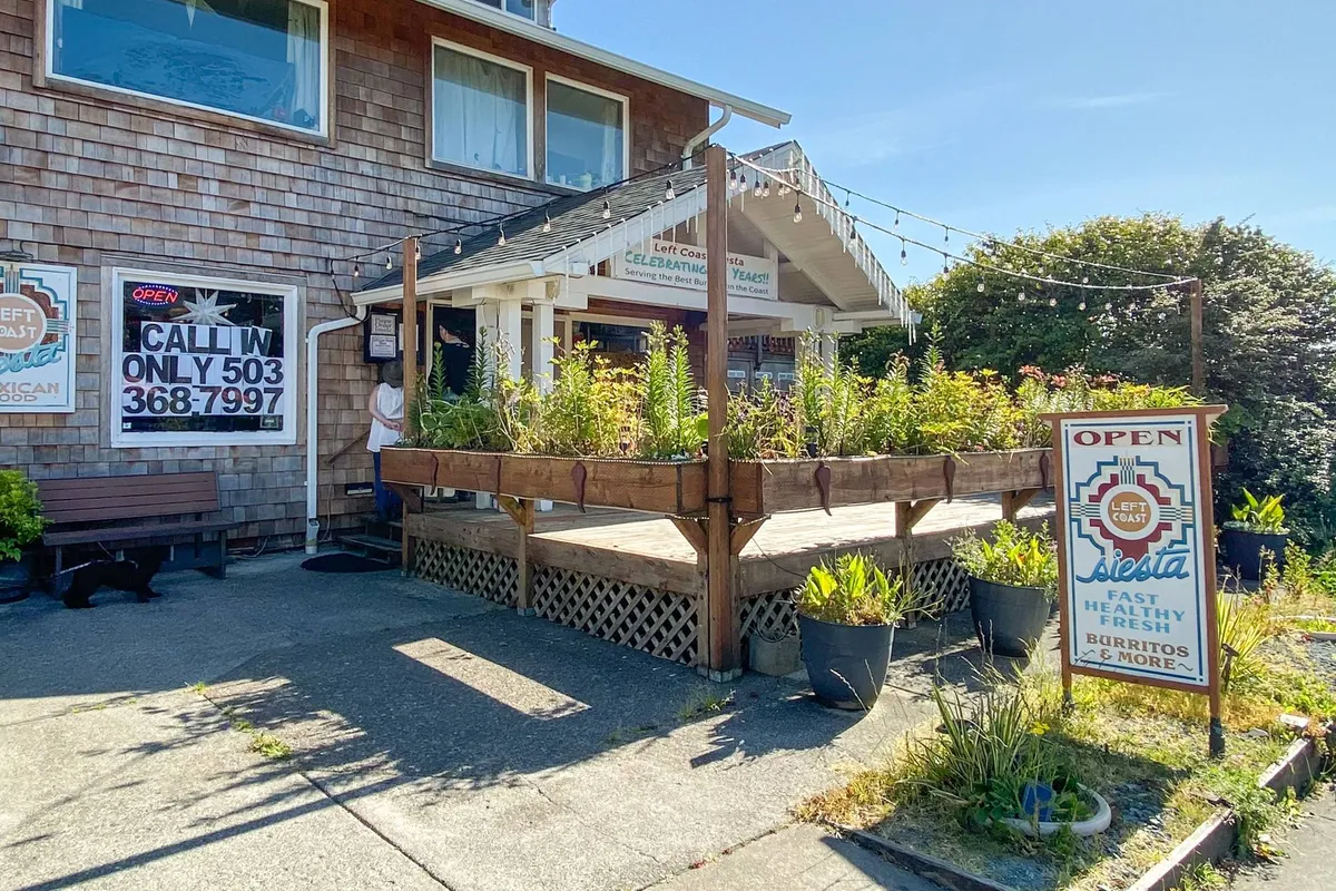 A welcoming wooden deck adorned with planters, a colorful sign, and hanging lights, inviting guests to dine outdoors. The open door adds a sense of hospitality, while the deck setting visually evokes summer picnics and gatherings.