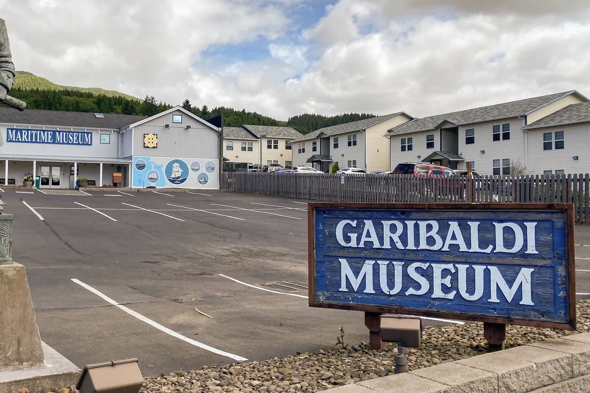 The exterior of the Garibaldi Maritime Museum, showcasing its welcoming sign, distinct architecture, and a statue near the entrance. The environment exudes a sense of curiosity and local history, inviting visitors to learn and explore.