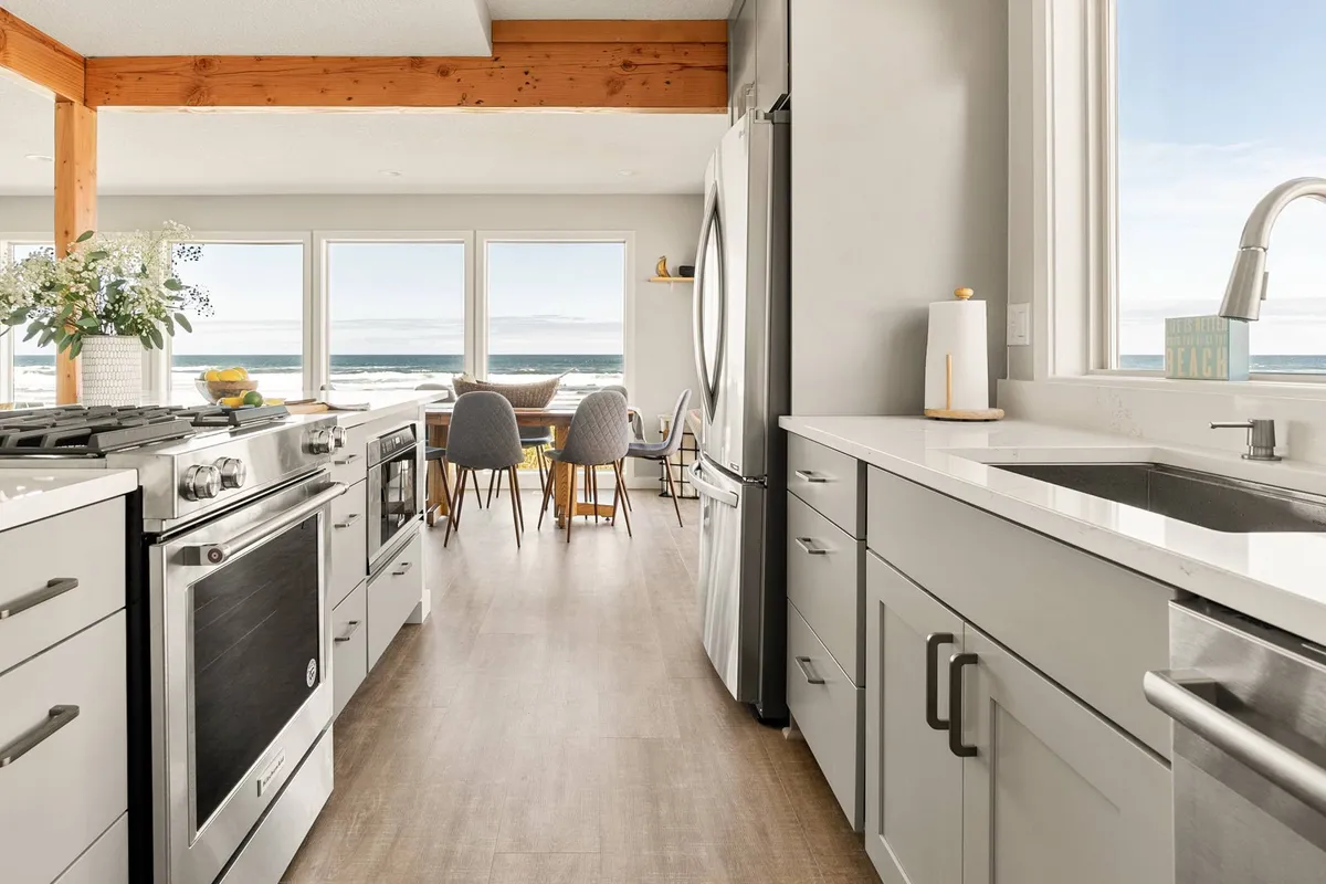 A bright, modern kitchen with high-end appliances, a spacious island with bar stools, and large windows that frame breathtaking ocean views. The kitchen seamlessly connects with the adjacent dining area, highlighting spaces for both meal preparation and entertaining guests.