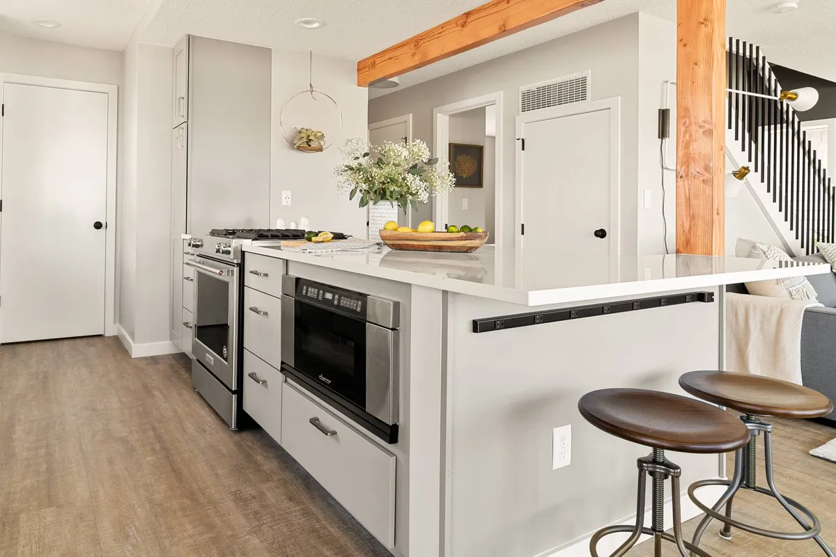 A modern kitchen with a central island, bar stools, contemporary appliances, and a fresh flower arrangement. The space is bright and inviting, highlighting energy-efficient appliances.