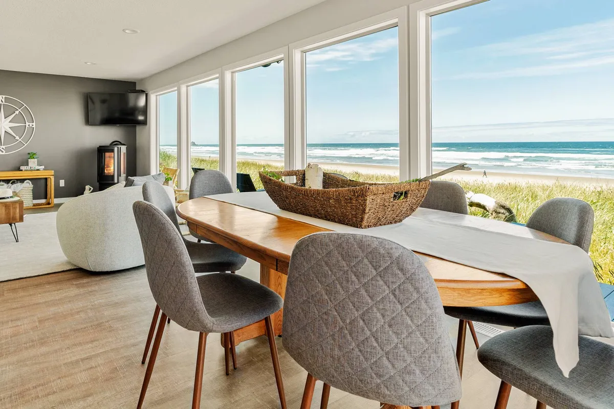 A tranquil yet welcoming dining area and cozy seating nook, both set against large picture windows framing stunning ocean vistas. The arrangement invites both intimate family meals and relaxed gatherings with friends, bathed in the glow of sunset or morning light.