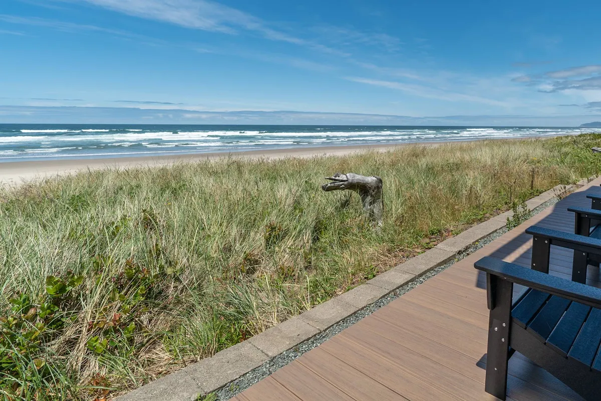 This image captures sweeping ocean waves with dune grass and driftwood in the foreground, accompanied by deck chairs that invite relaxation. The tranquil morning light and unobstructed view of the water evoke an immersive seaside experience.