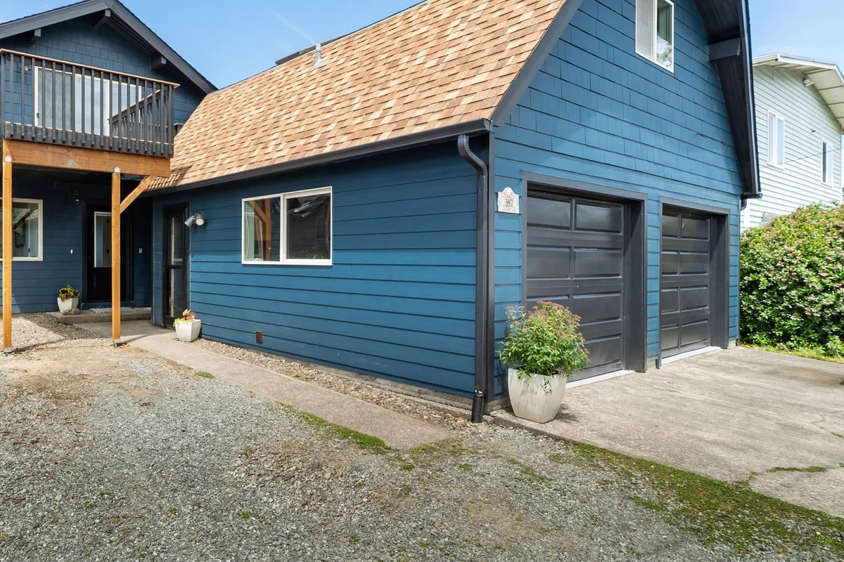 The blue exterior of Seas the Day with a wooden porch and visible garage door. The exterior view hints at the property's accessible entry and convenient parking, possibly including EV charging facilities.