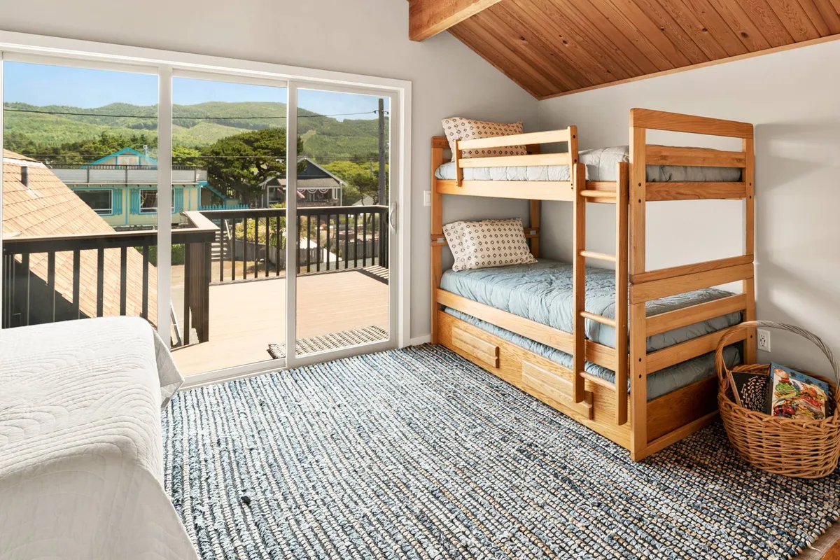 A playful bedroom with a classic bunk bed, large window, and woven rug. The room is brightened by natural light and designed for both comfort and fun, making it perfect for families or groups of friends.